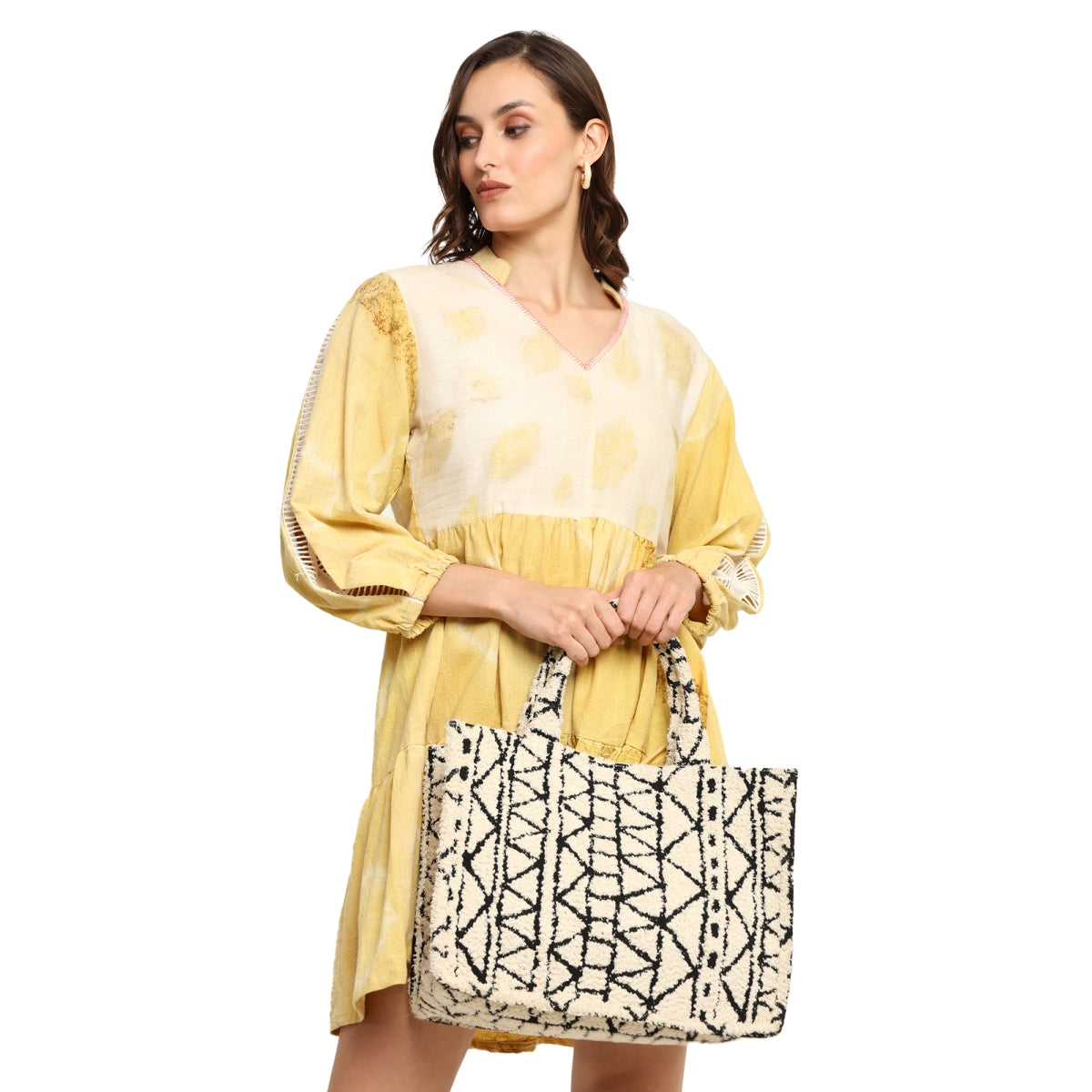 A woman wearing a yellow dress holding a black and white patterned box bag.